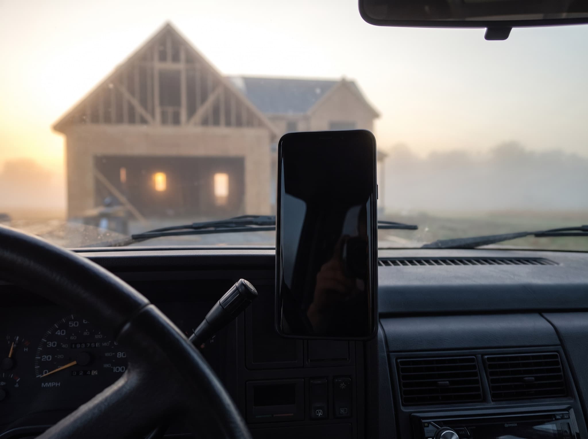 A phone mounted on a truck dashboard, a framed house in the fog beyond the windshield